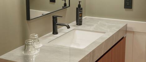 A modern bathroom with a marble sink, two wall-mounted lamps, a mirror, and a towel rack.