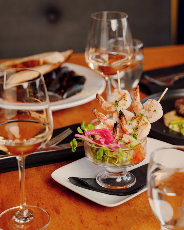 A dining table with a glass bowl containing shrimp skewers, a plate of food, and wine glasses.