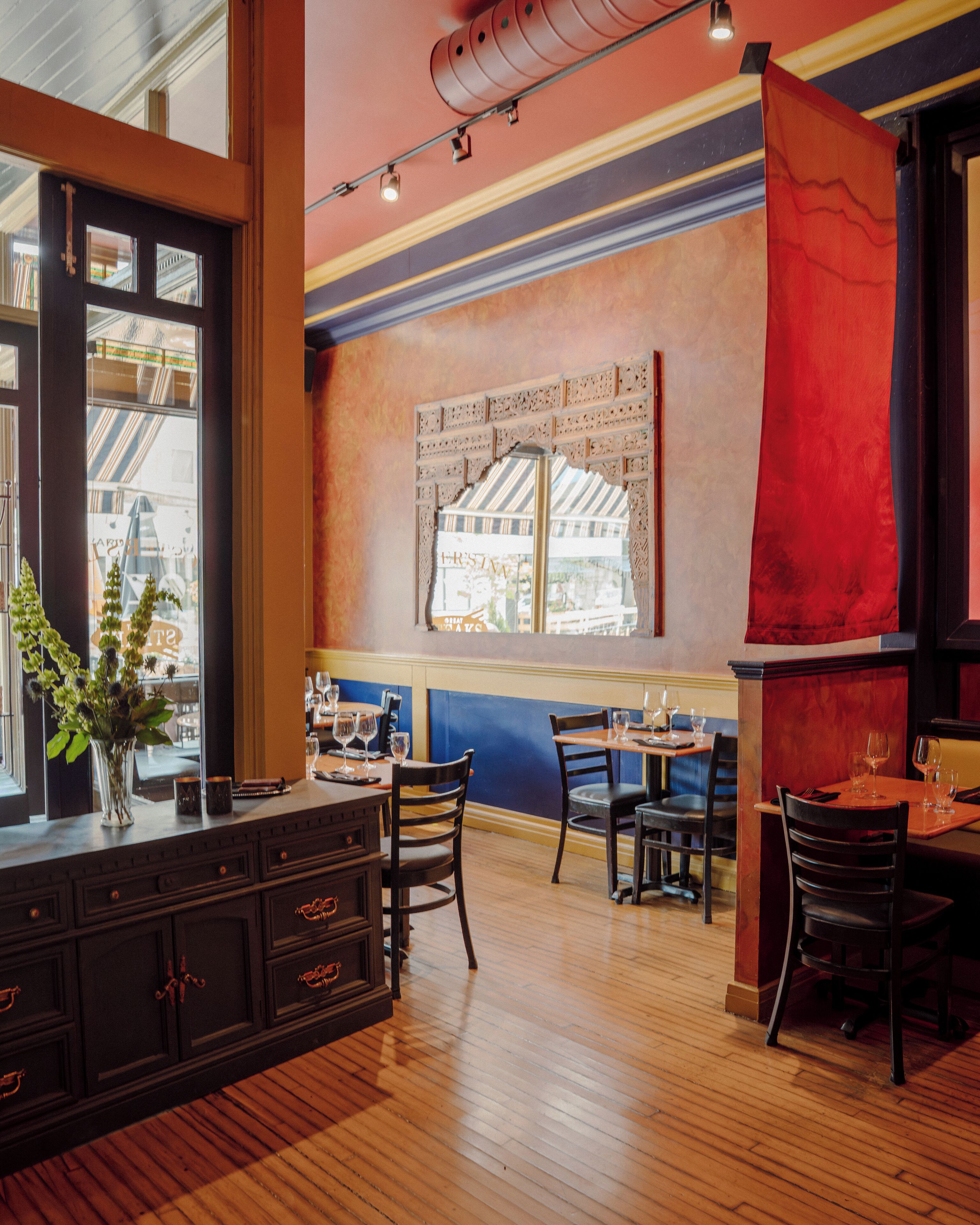 L’intérieur d’un restaurant, avec un plancher en bois, des meubles en bois foncé et une grande fenêtre donnant sur la rue.