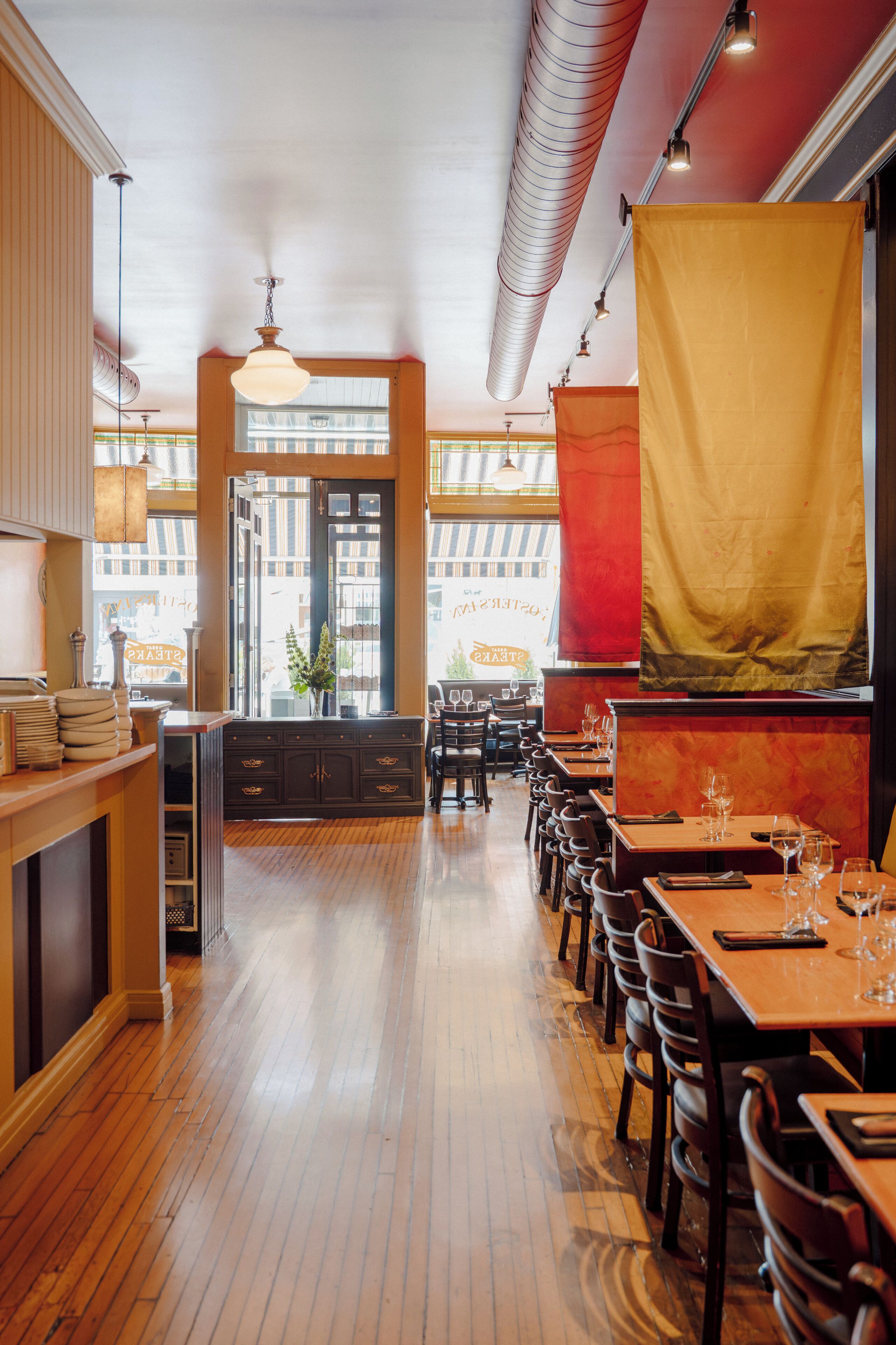 A restaurant interior with wooden flooring, tables, chairs, and a view through the window.