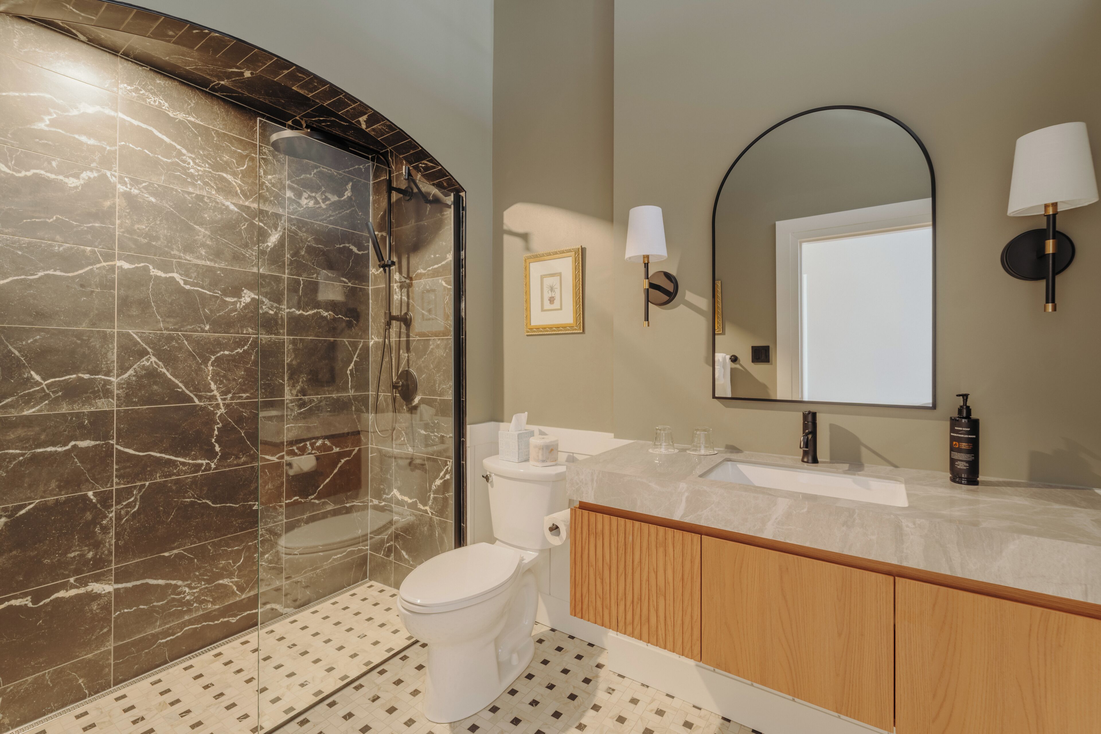 Un baño moderno con ducha de mármol, inodoro, lavabo y espejo.