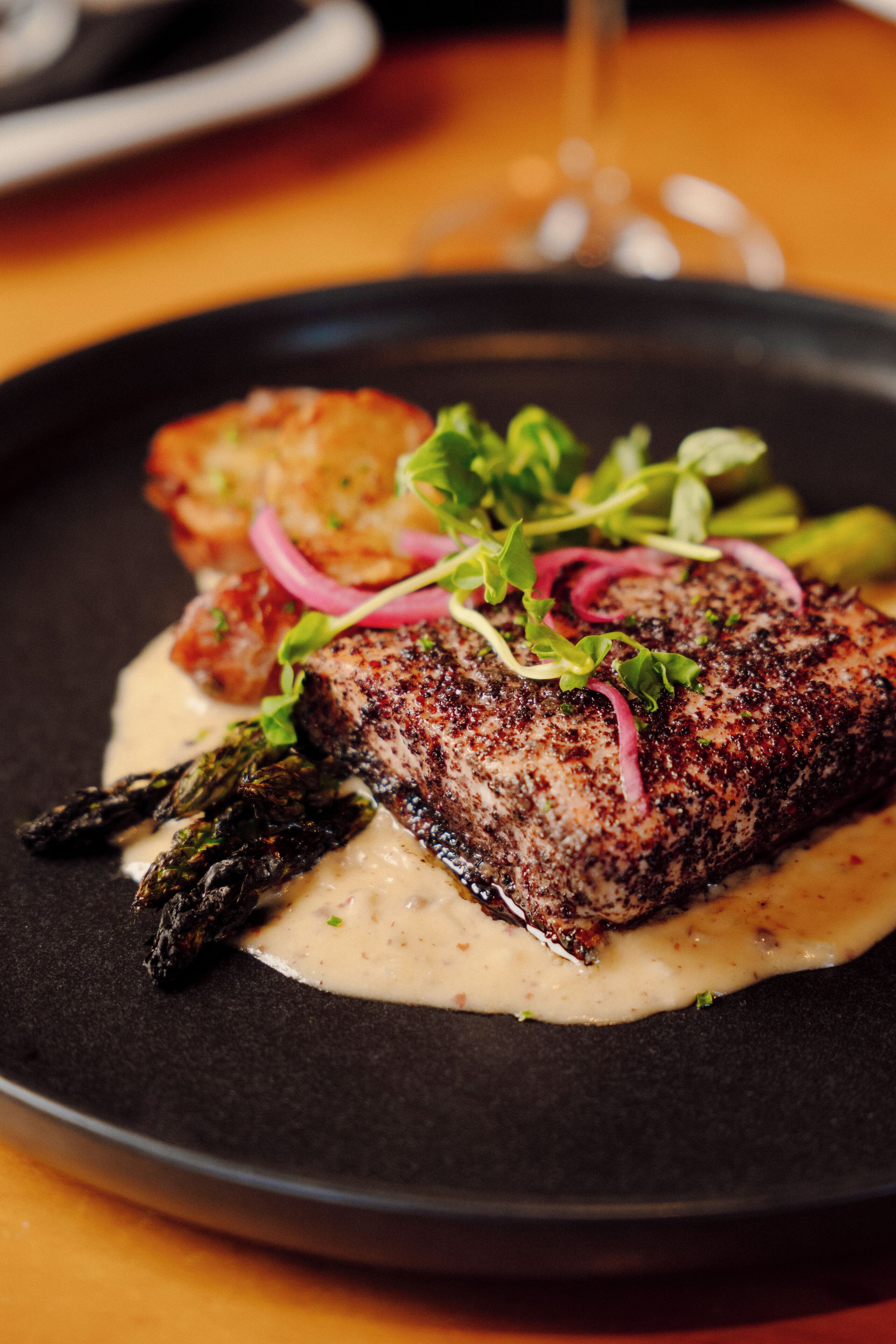A plate of food with a steak, asparagus, and a creamy sauce.
