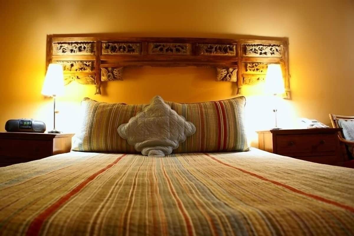 A hotel room with a bed, two bedside lamps, a clock, and a decorative headboard.