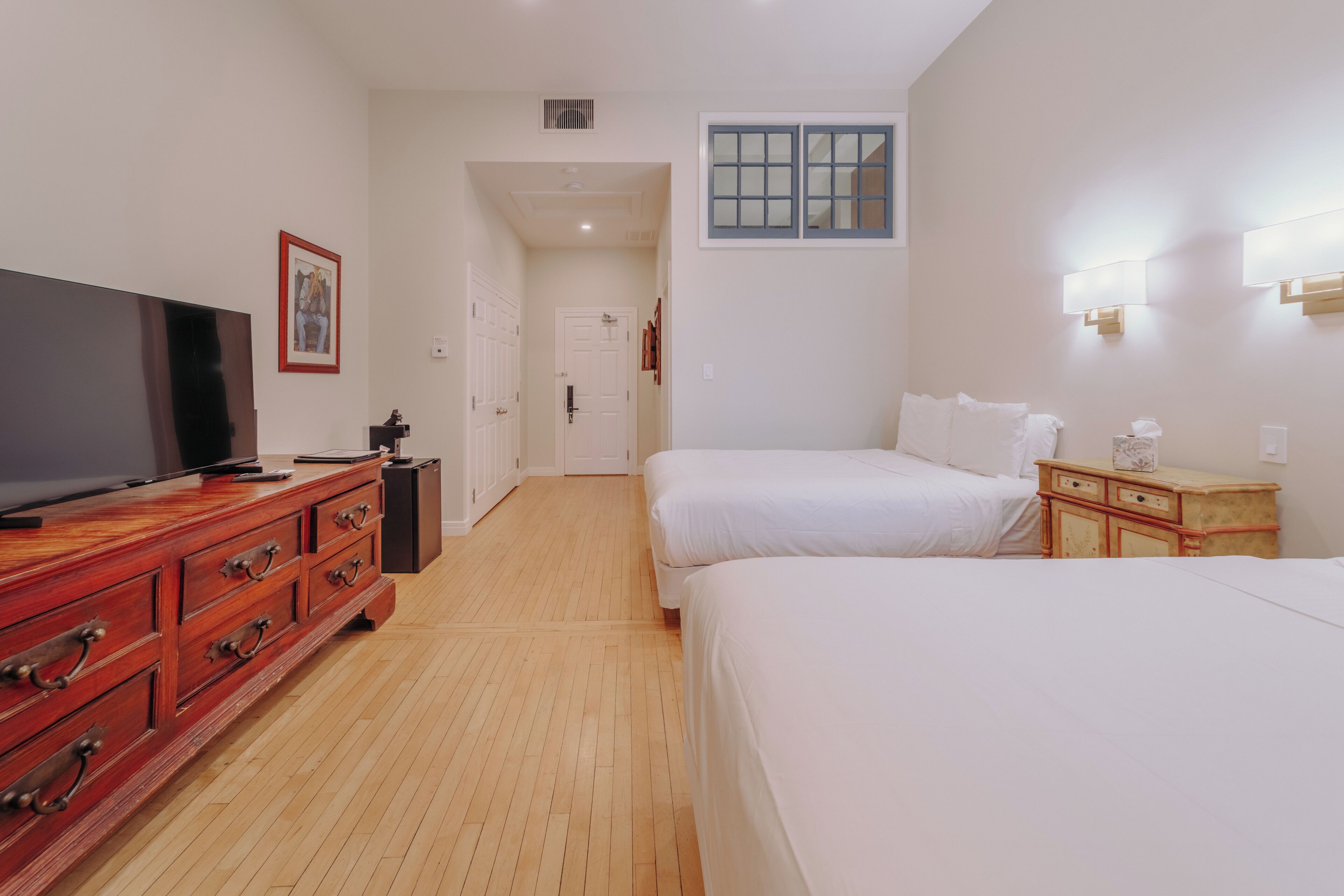 A hotel room with two beds, a TV on a wooden dresser, and a hallway leading to another room.
