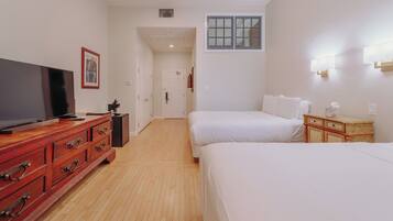 A hotel room with two beds, a TV on a wooden dresser, and a hallway leading to another room.
