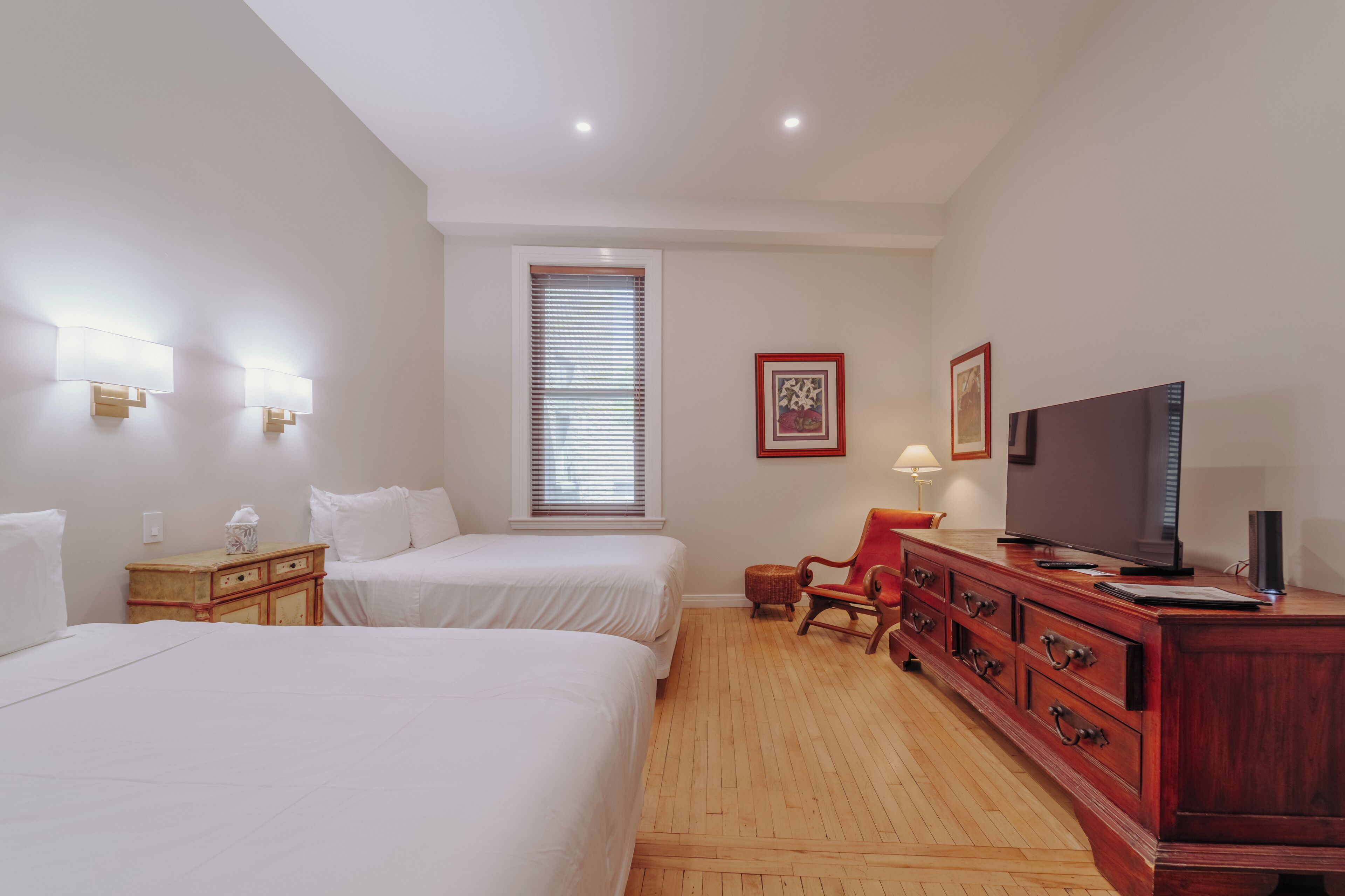 Habitación de hotel con dos camas, un aparador de madera, un televisor y una ventana con persianas.