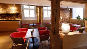 A restaurant interior with stone walls, wooden beams, and red chairs. Tables are arranged for dining.