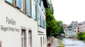 A building named 'Pavillon Régent Petite France' with a river and colorful houses in the background.