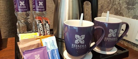 A tray with two purple mugs, two water bottles, a coffee maker, and various snack packets.
