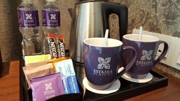 Una bandeja con dos tazas moradas, dos botellas de agua, una cafetera y varios paquetes de aperitivos.