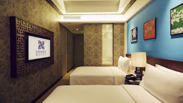 A hotel room with two beds, a TV mounted on a decorative panel, and a wall with framed artwork.
