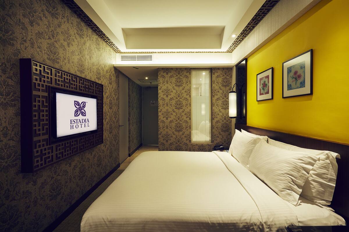 A hotel room with a bed, a TV mounted on the wall, and two framed pictures on the wall.