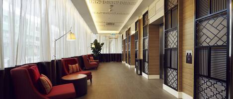 A hotel lobby with red seating, a large plant, and traditional wooden partitions.