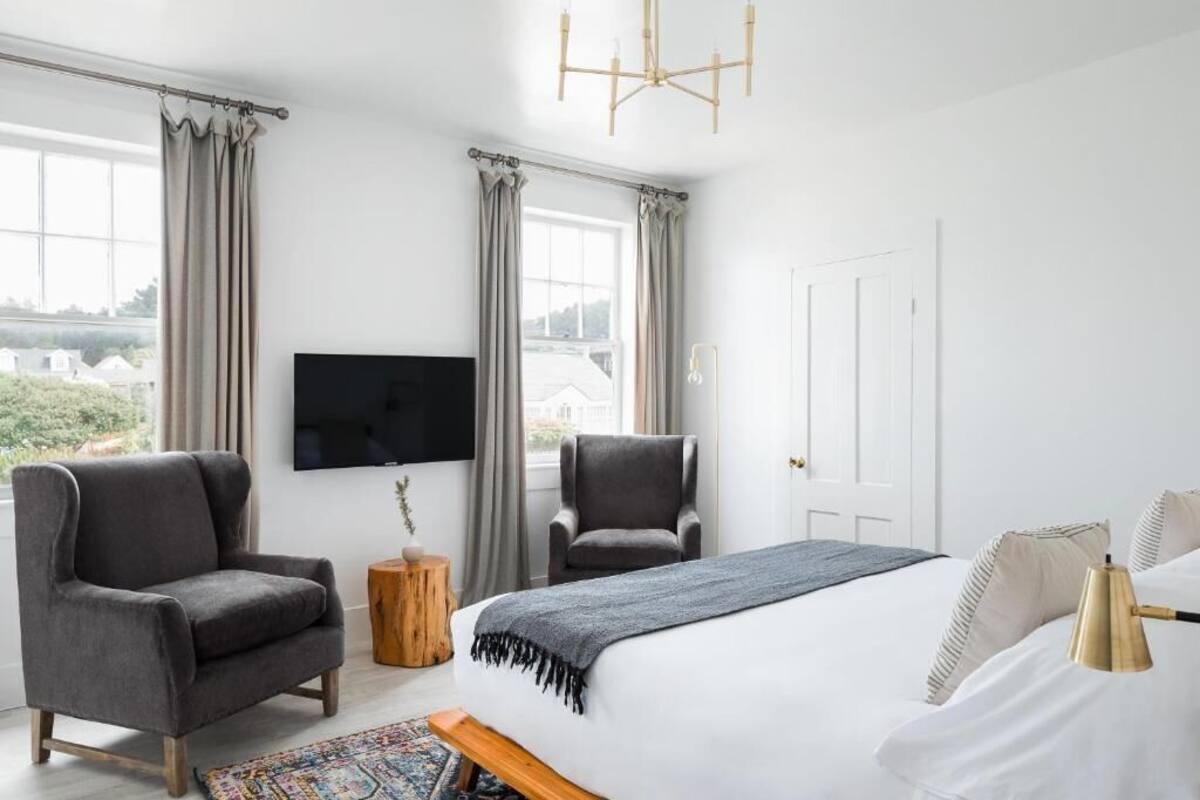 Un dormitorio moderno con una cama grande, dos sillones, un televisor y vistas al exterior.