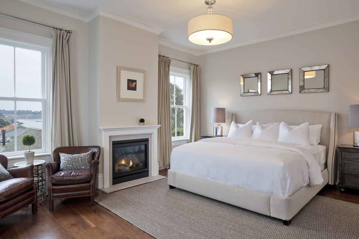 Un dormitorio con una cama grande, chimenea, sillón de cuero y vistas al exterior.