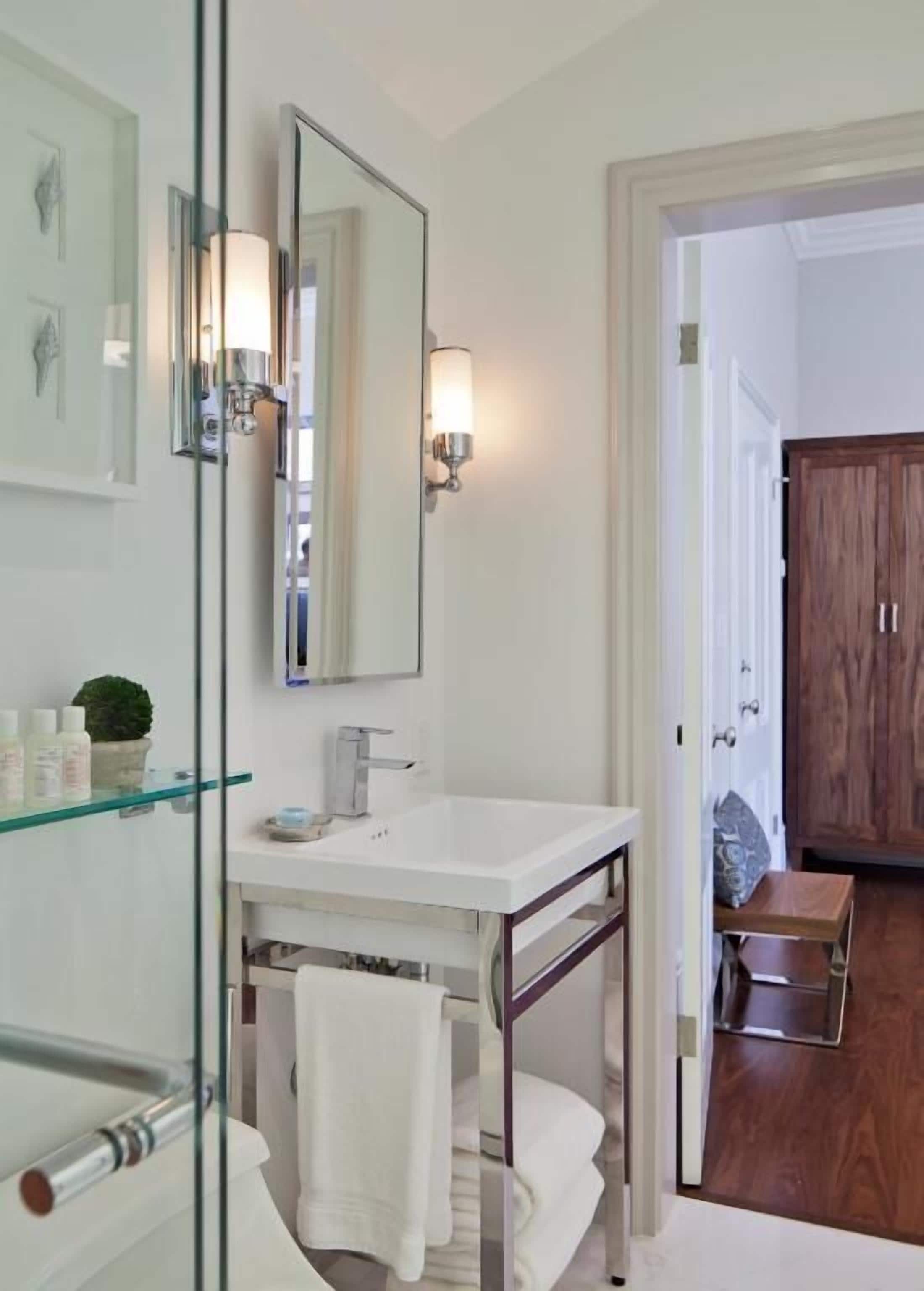 A modern bathroom with a glass shower enclosure, a white sink, and a wooden door in the background.