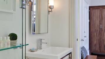 A modern bathroom with a glass shower enclosure, a white sink, and a wooden door in the background.
