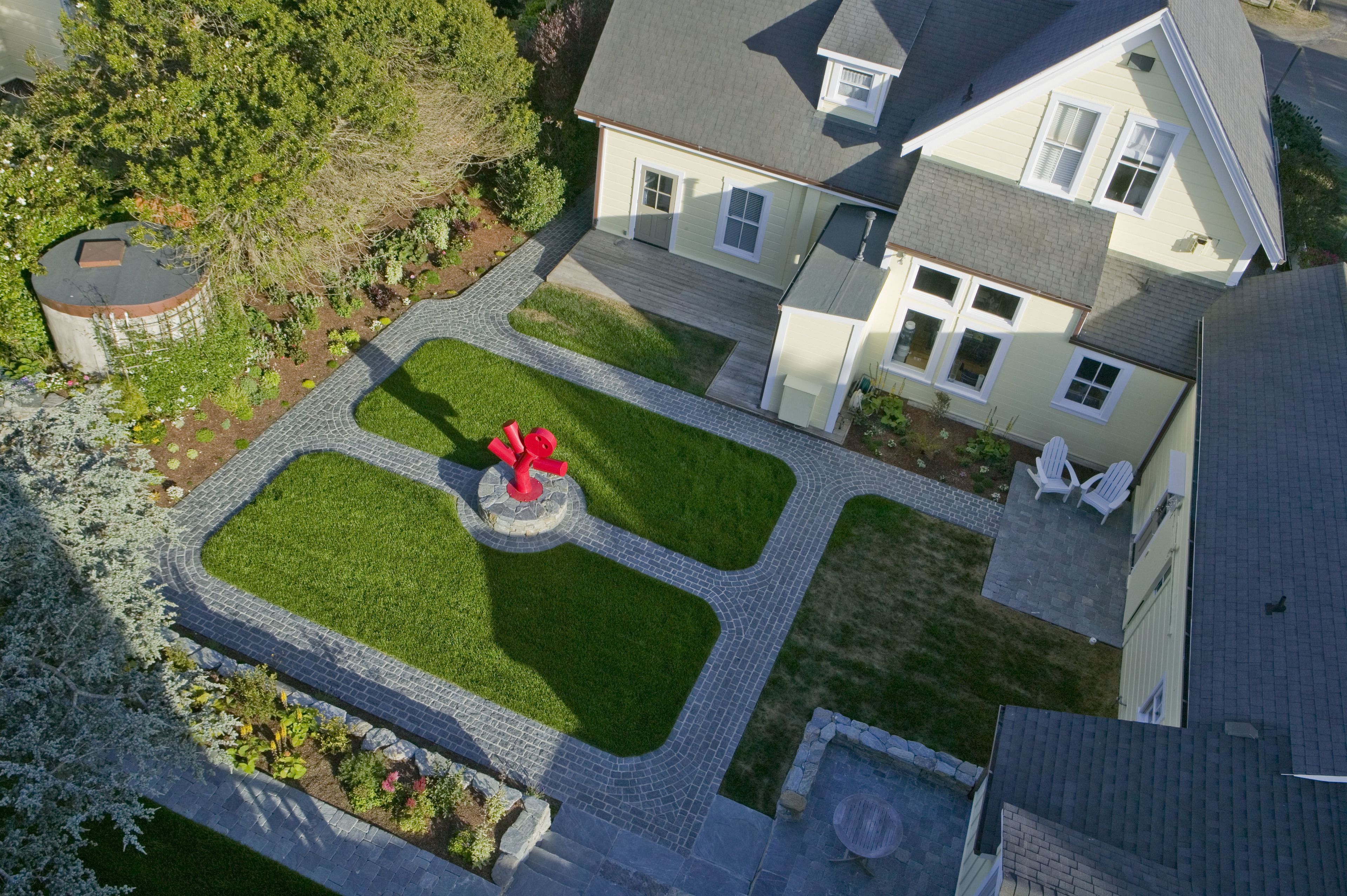 An aerial view of a residential property with a landscaped garden, a circular red sculpture, and a two-story house with a grey roof.