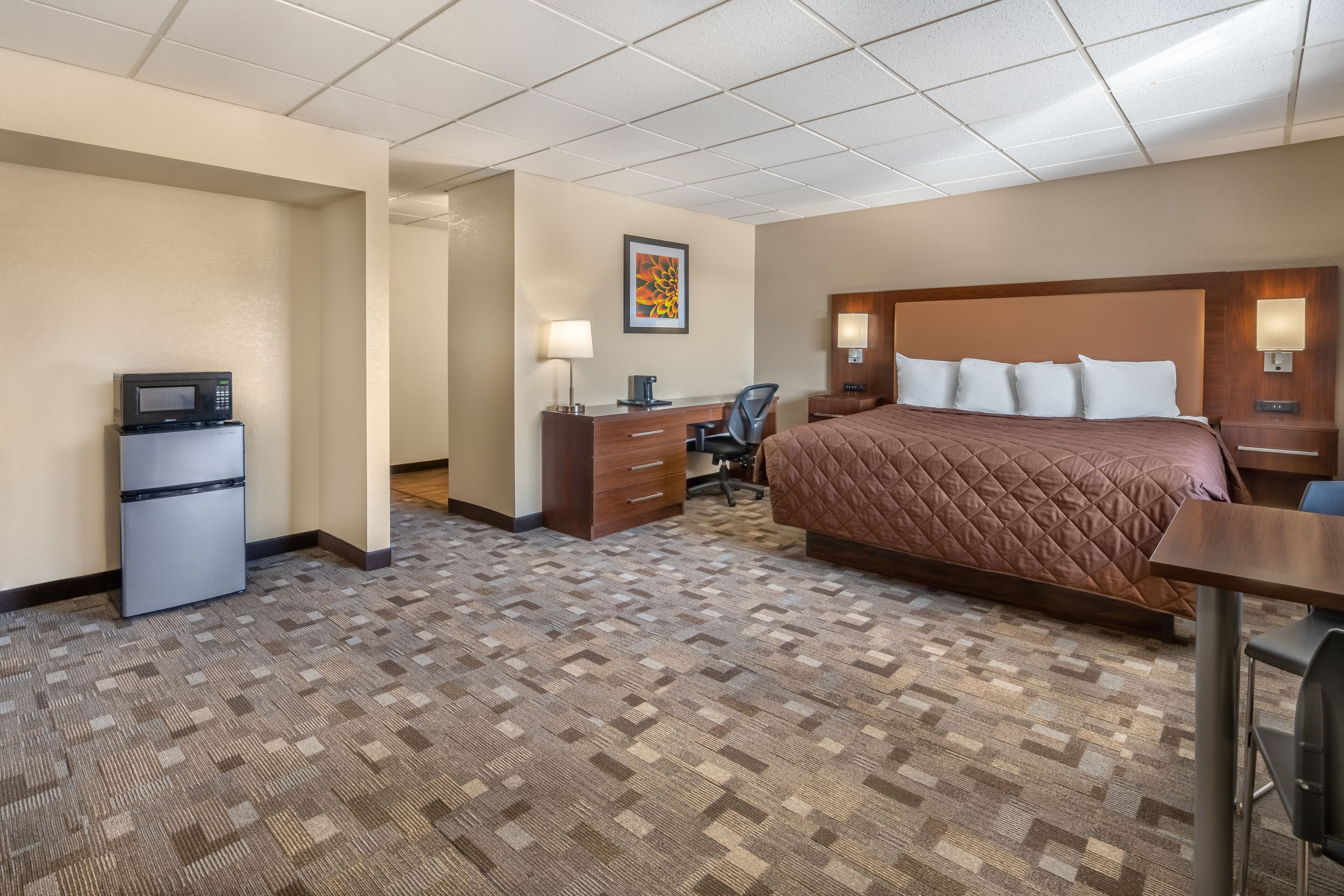 A hotel room with a bed, desk, chair, and a microwave on a mini-fridge.