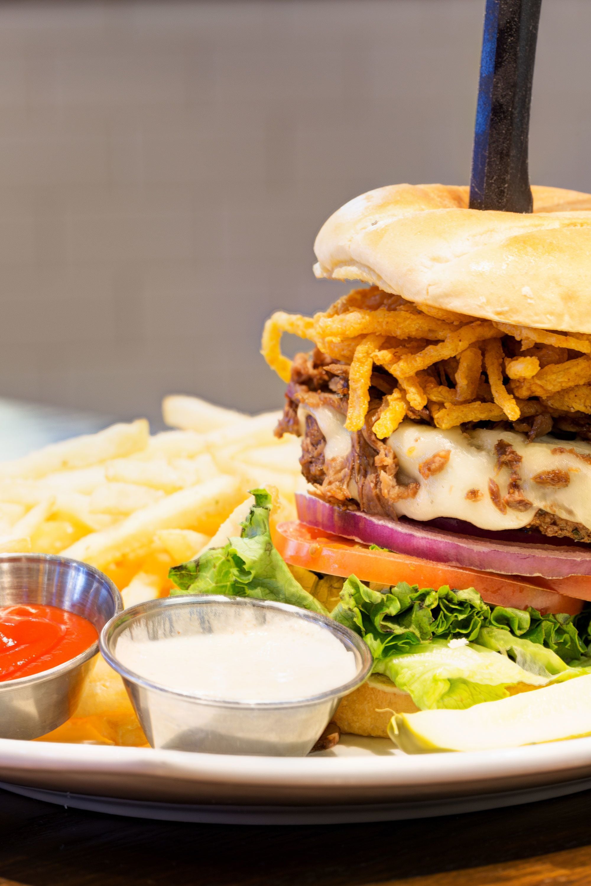 A burger with fries and two dipping sauces on a plate.