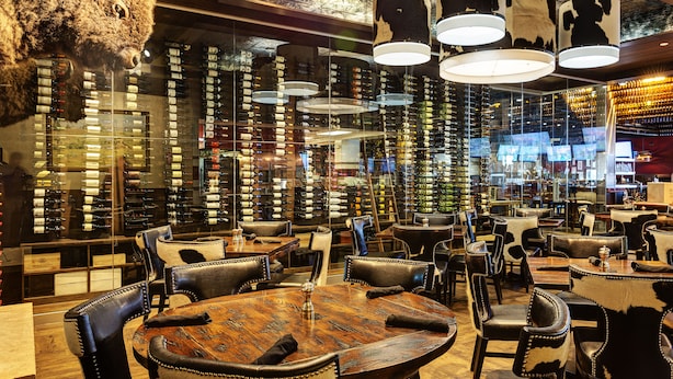 Un restaurante con sillas de cuero, mesas de madera y una pared llena de botellas de vino.