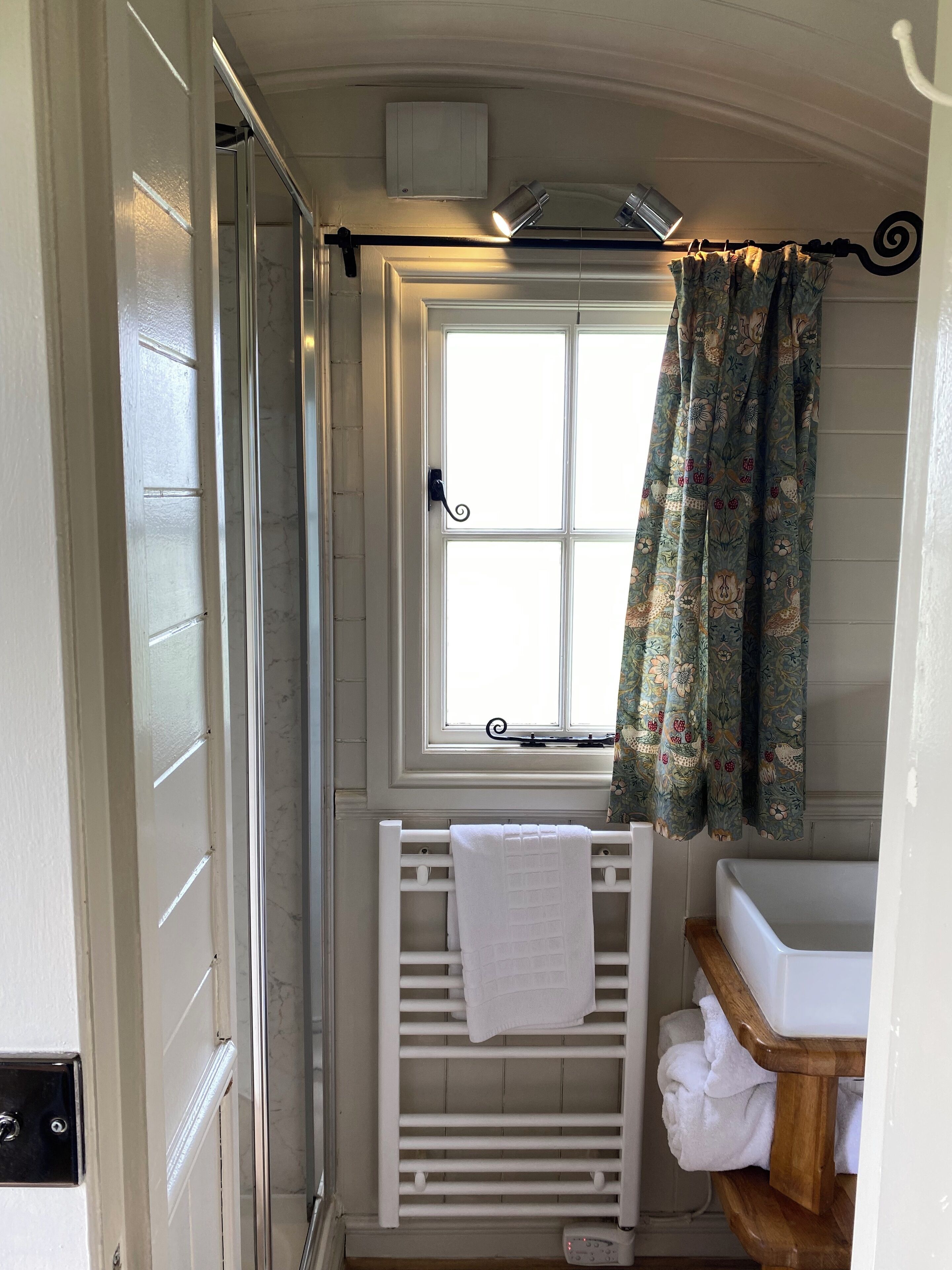 A bathroom with a white radiator, a window with a curtain, a white towel on the radiator, and a wooden vanity with a sink.