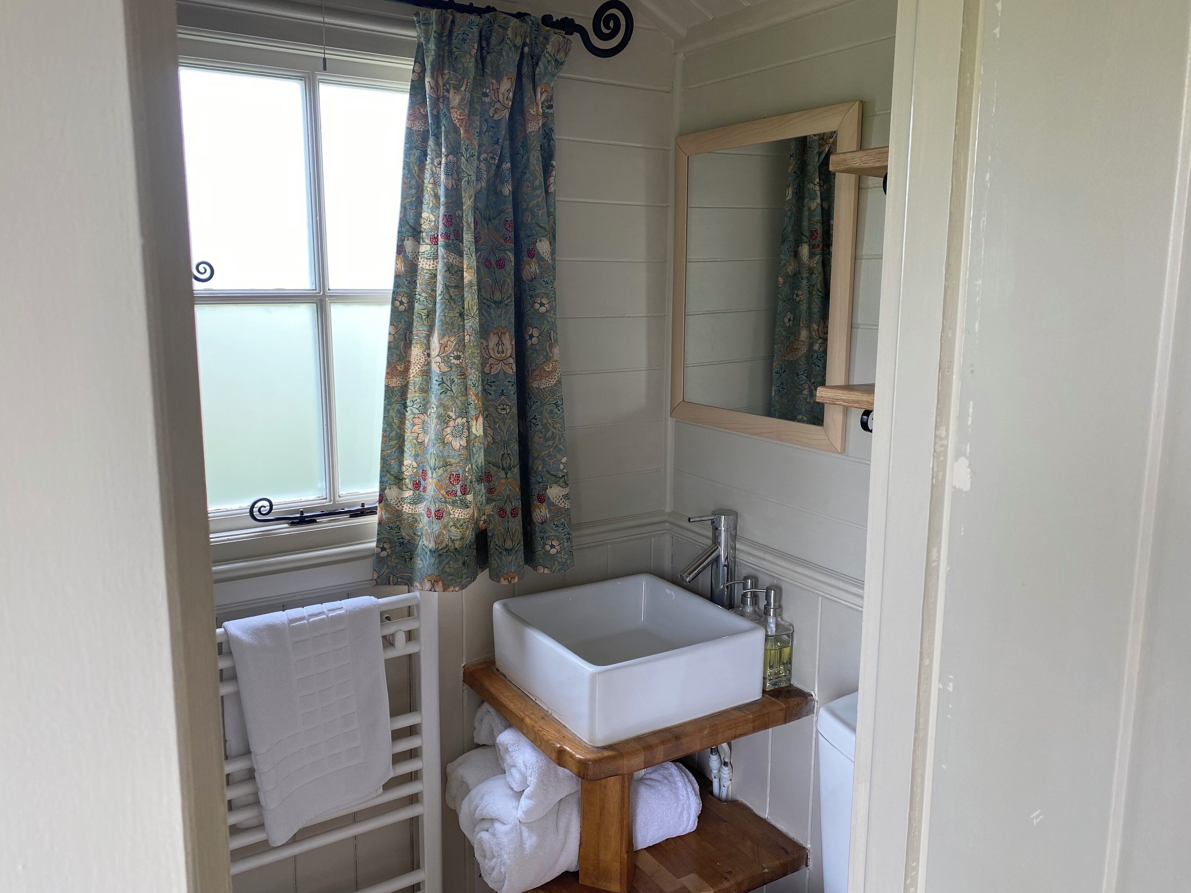 Un baño con ventana, lavamanos blanco, espejo y perchero.