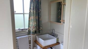 Un baño con ventana, lavamanos blanco, espejo y perchero.