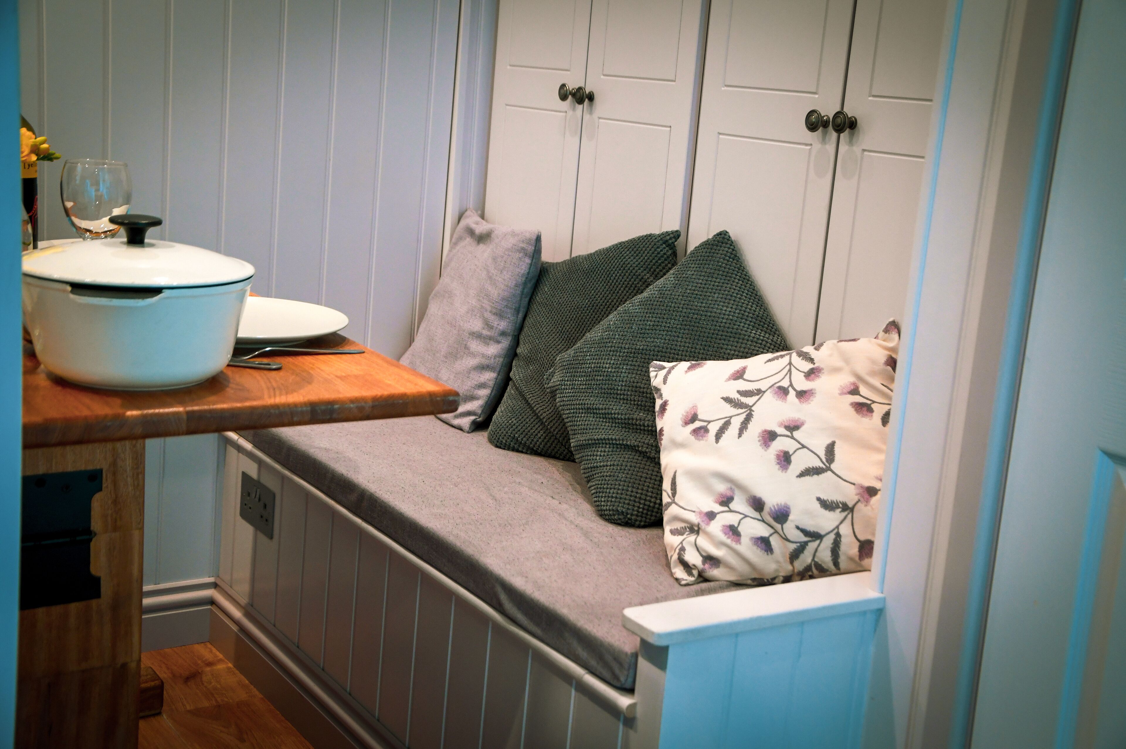 A narrow kitchen with a built-in bench, a pot on the counter, and a wine glass.