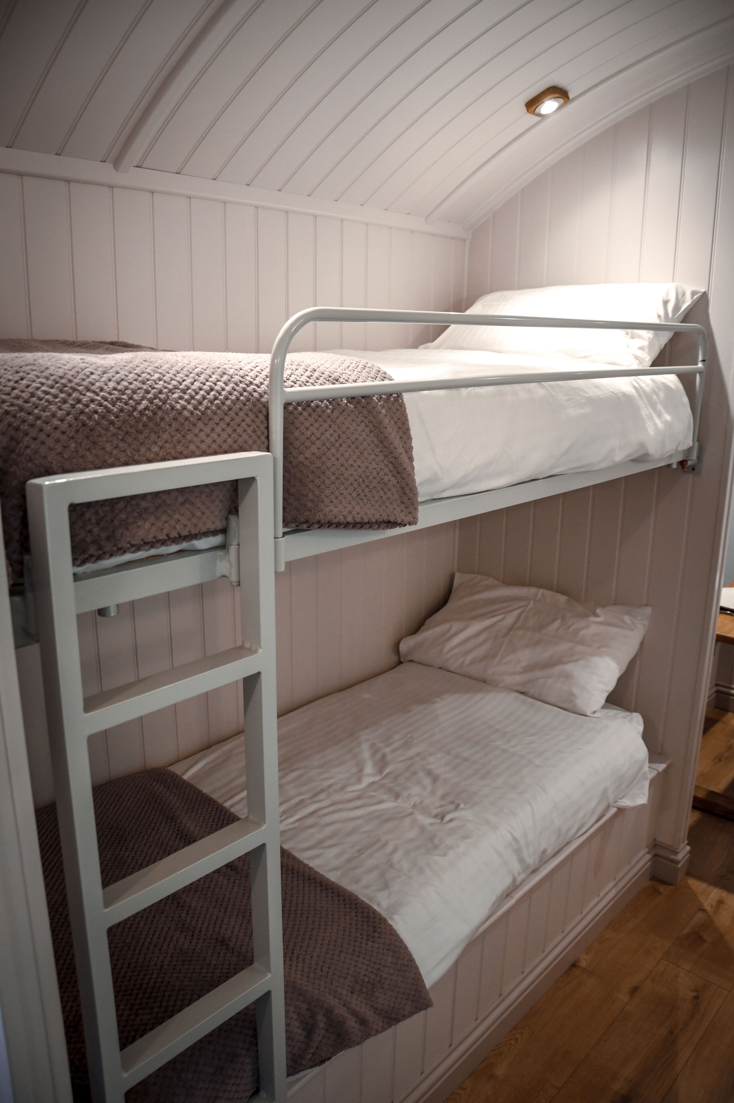 Camera con letto a castello, pareti bianche e pavimento in legno.