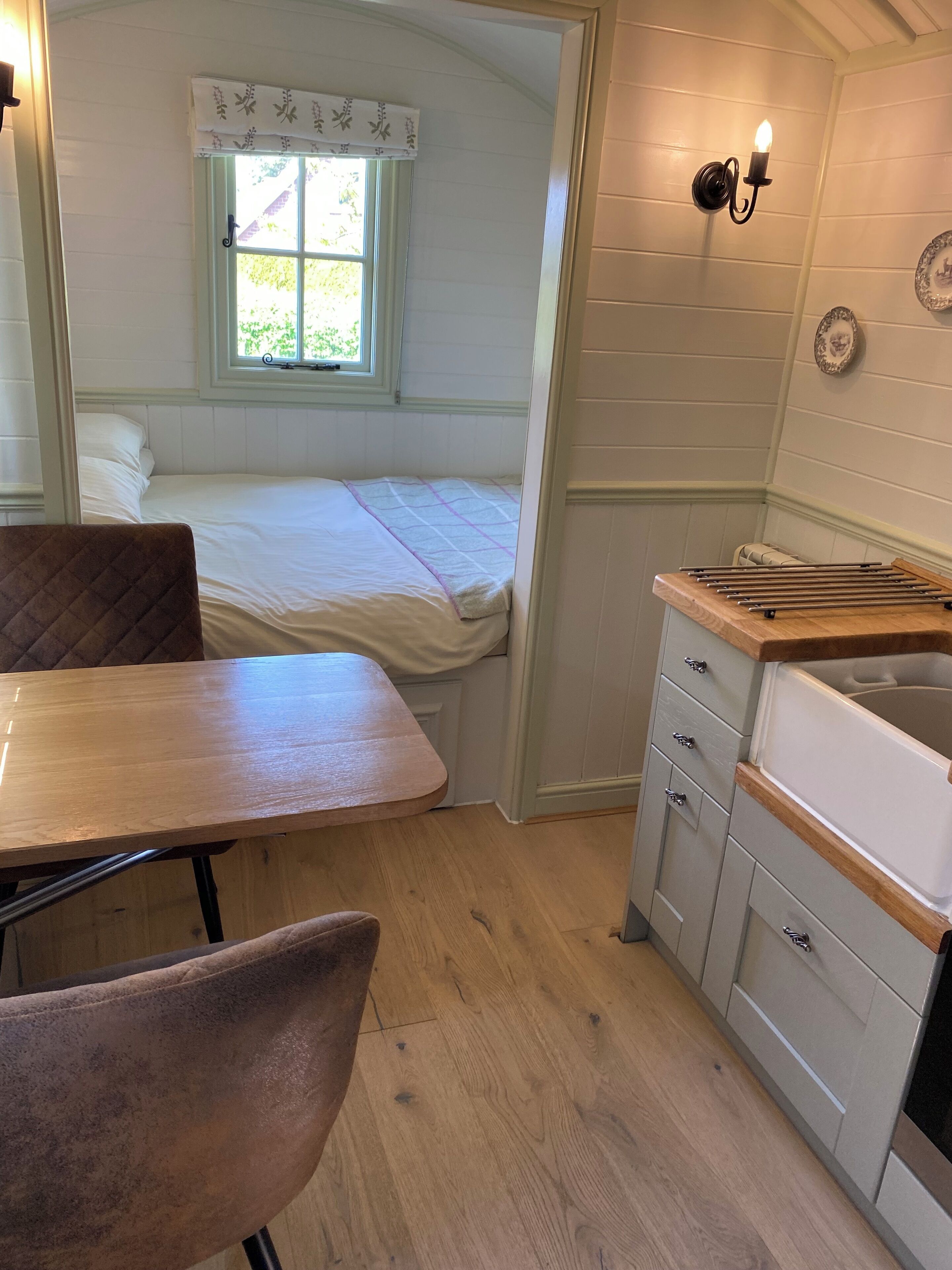 Una habitación pequeña con cama, mesa, silla, lavamanos y ventana.