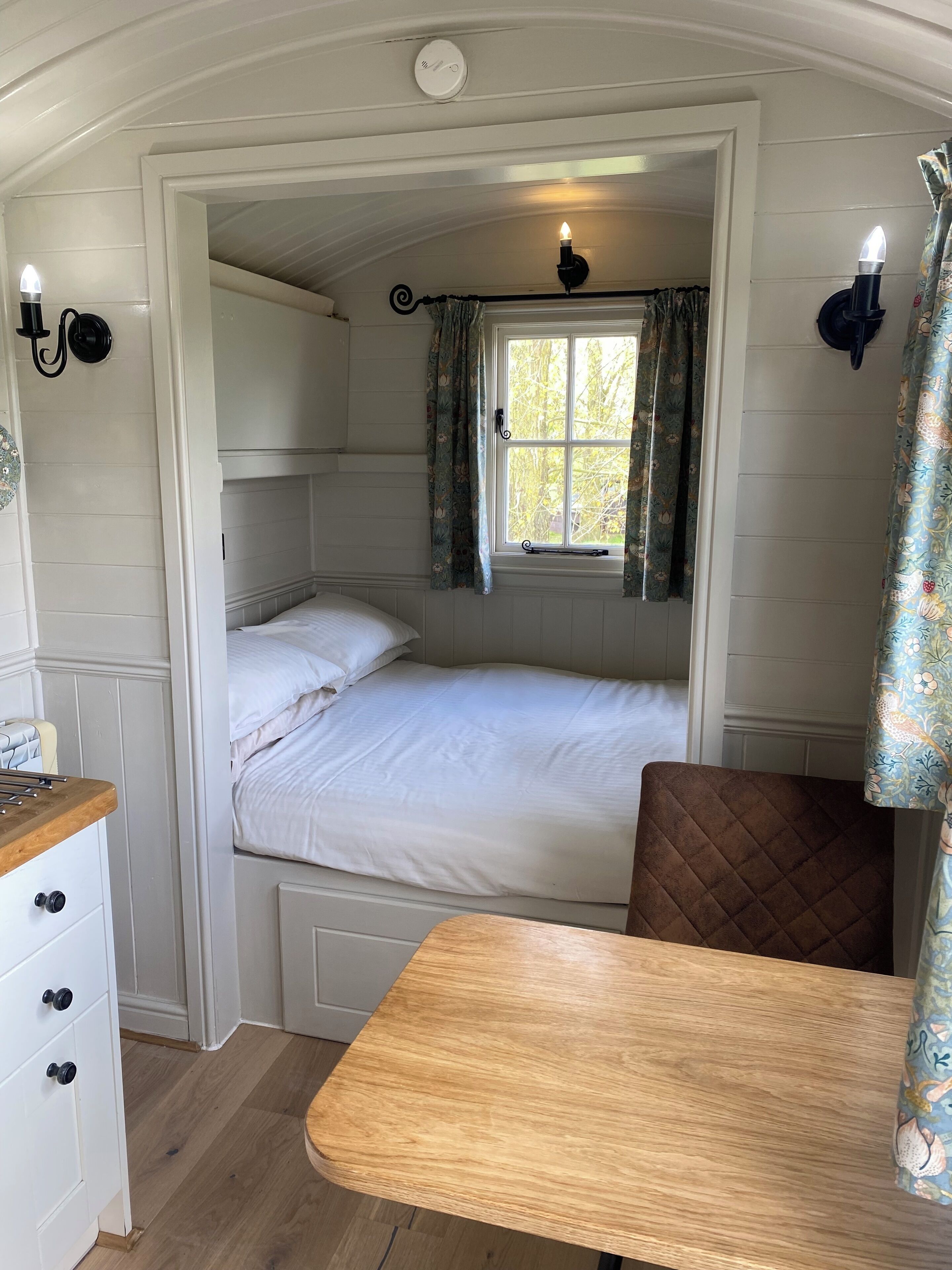 A cozy bedroom with a bunk bed, a small table, and a window with curtains.