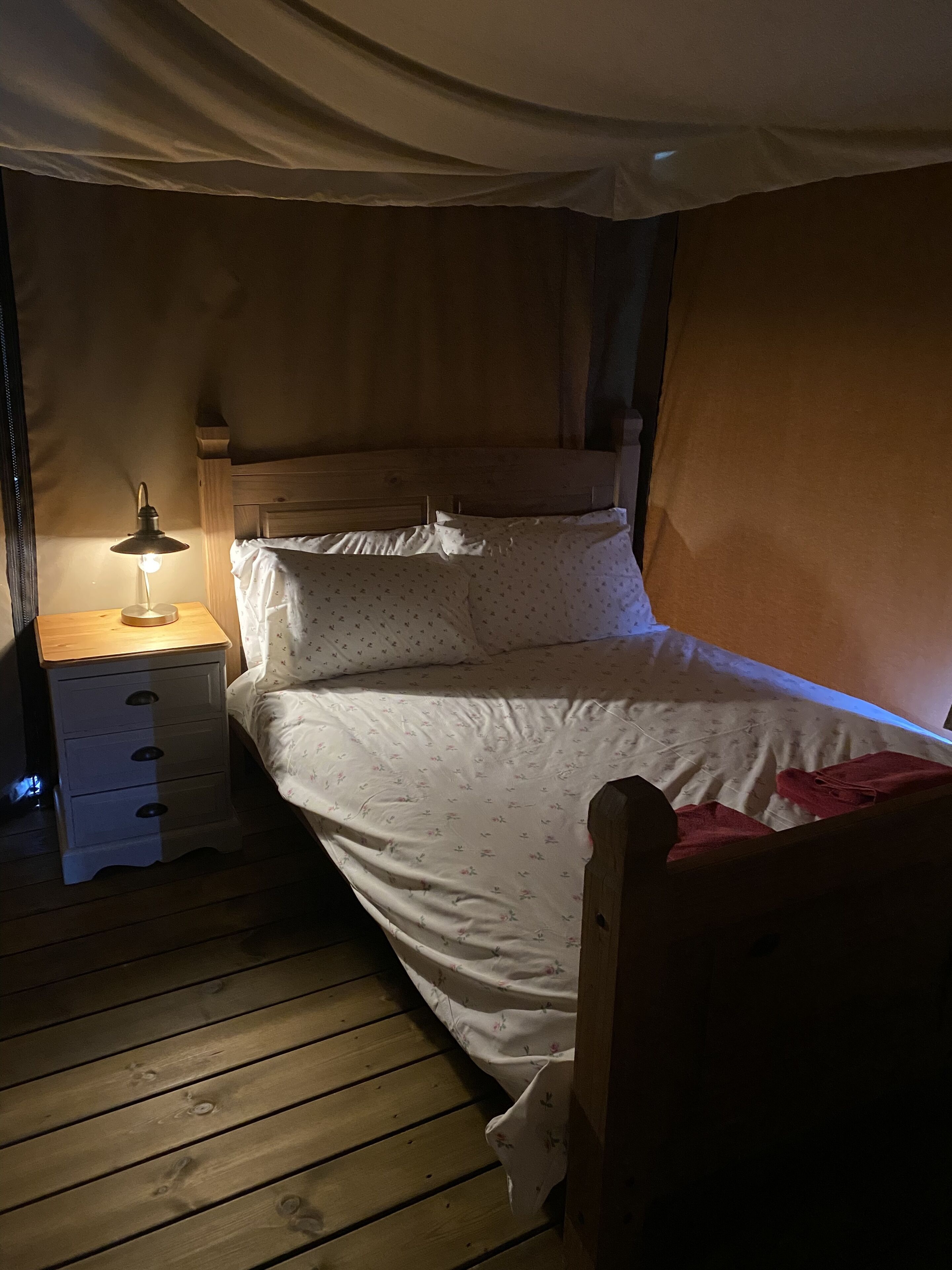 Un lit simple avec une tête de lit en bois, une table de chevet avec une lampe et un plancher en bois.