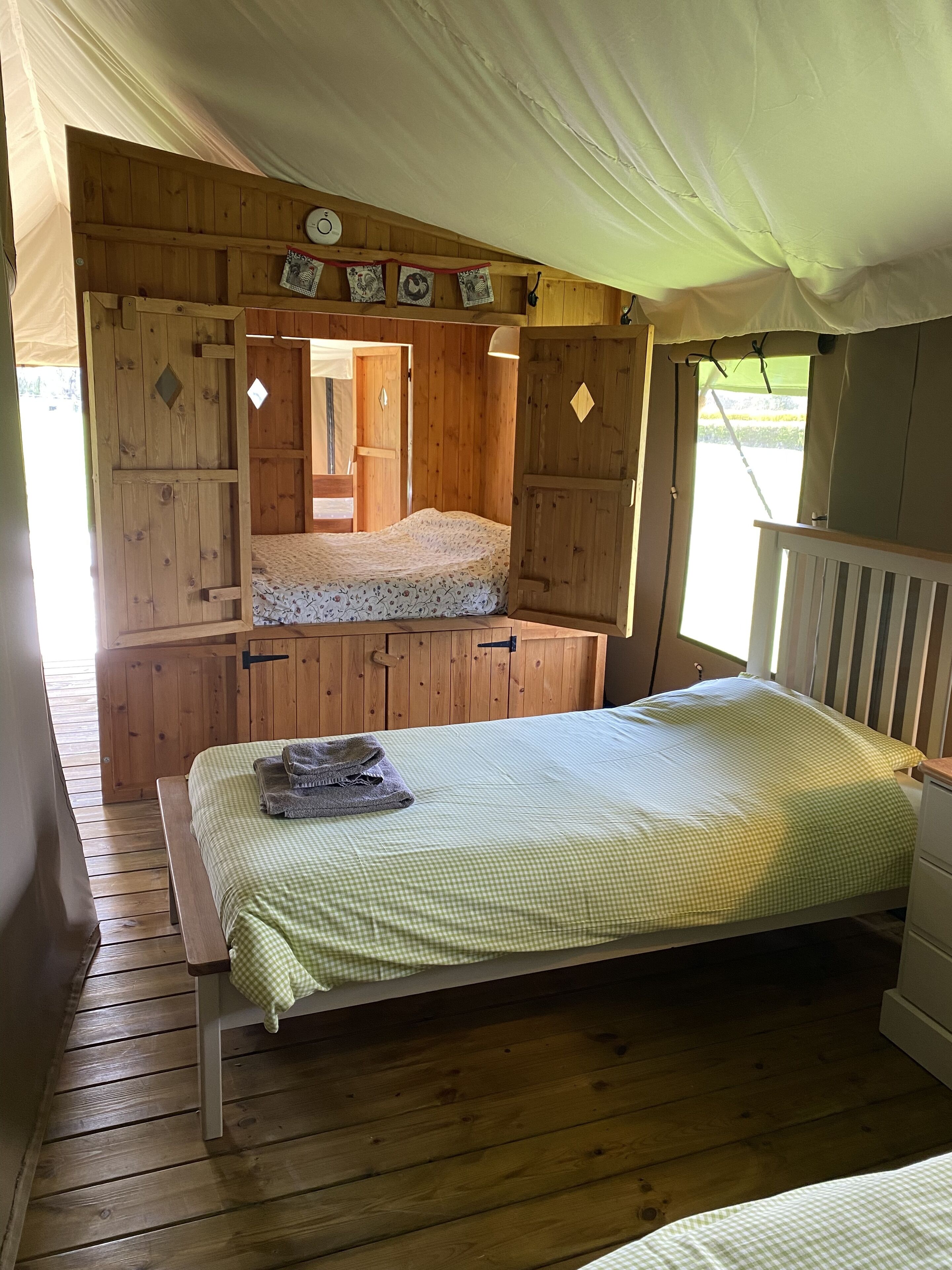 Une cabane en bois avec un lit simple, un petit banc et une armoire en bois.