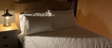 A single bed with floral bedding, a bedside table with a lamp, and a wooden headboard.