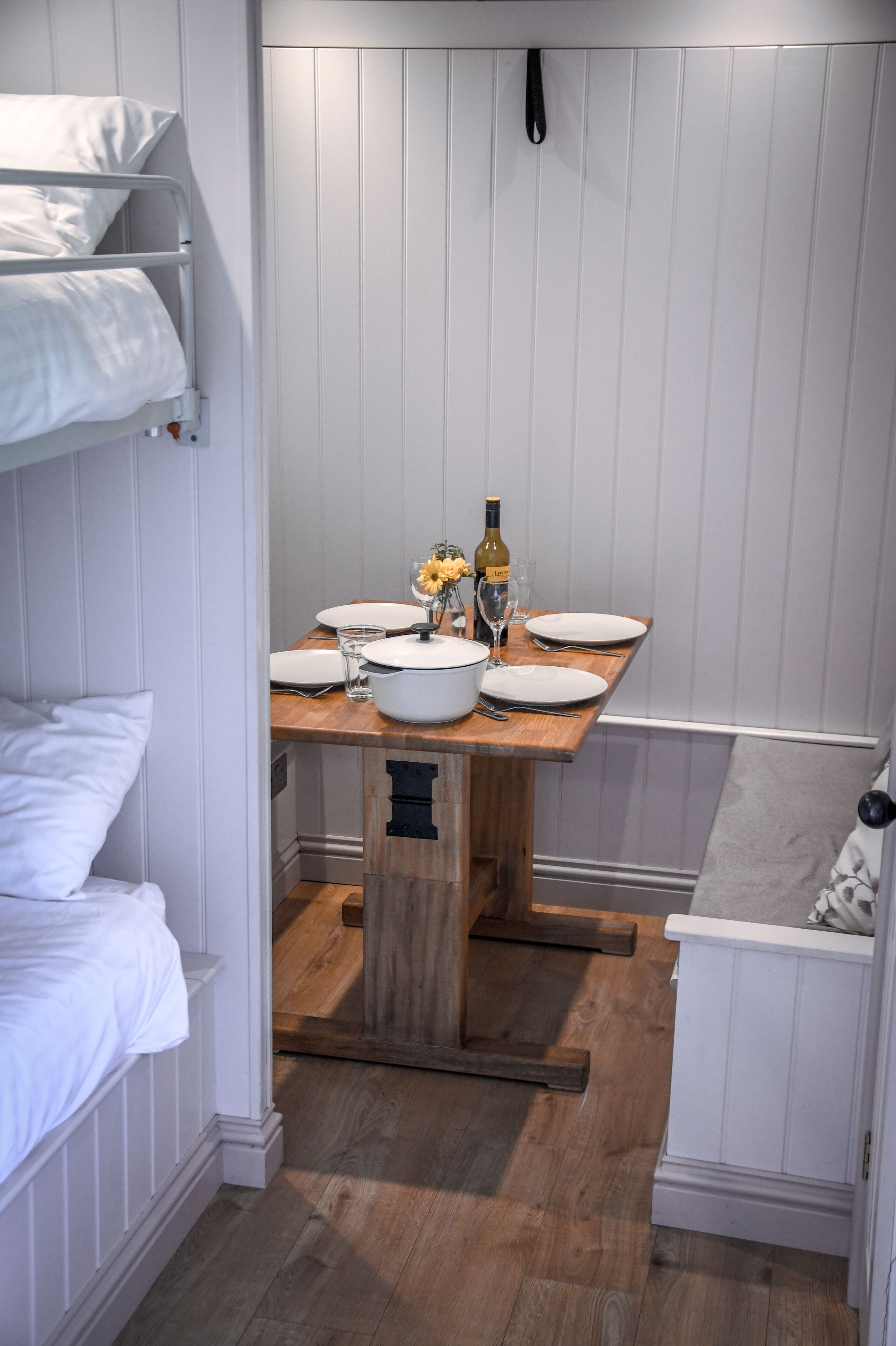 Ein kleines Zimmer mit Etagenbett, einem Holztisch gedeckt mit Tellern, Gläsern und einer Flasche, sowie einem kleinen Schrank.