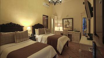 Une chambre d’hôtel avec deux lits, un bureau, une chaise, une télévision et un lustre.