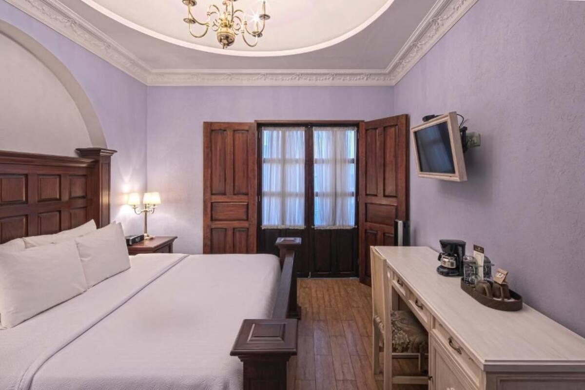 Habitación de hotel con una cama grande, cabecera de madera, un escritorio con computadora y televisión en la pared.