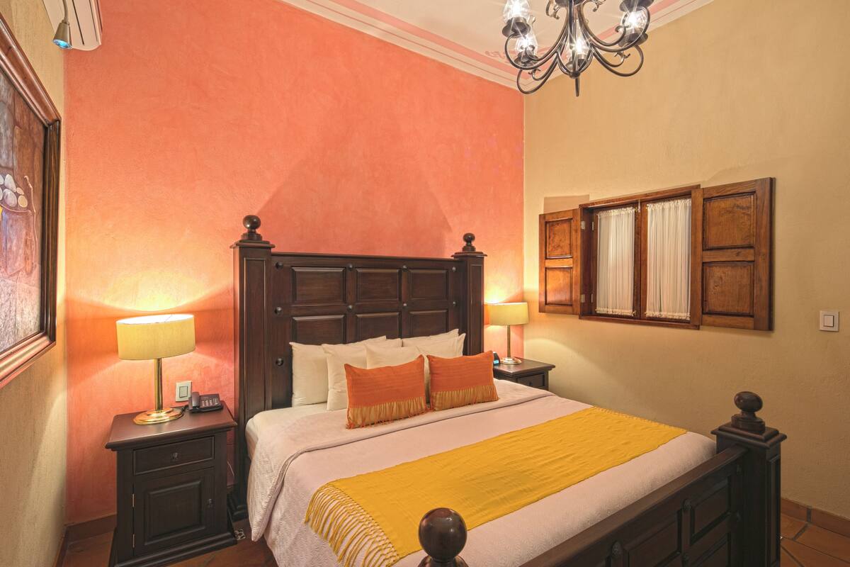 Habitación de hotel con una cama grande, dos mesitas de noche con lámparas, un cabecero de madera y una ventana con cortinas.