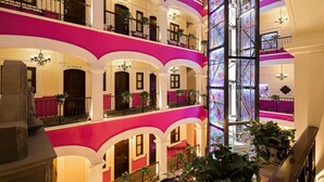 Un lobby de hotel con varios niveles, balcones, candelabros y plantas en macetas.