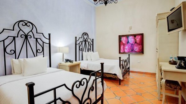A hotel room with two beds, a desk, a chair, a TV, and a wall with a floral painting. - Casona María (Puebla)