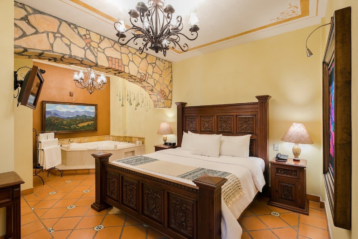 A bedroom with a large bed, a stone wall, a chandelier, and a painting.