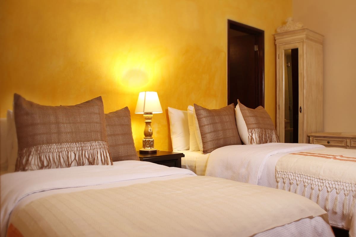 A hotel room with two beds, a nightstand with a lamp, a wardrobe, and a door.