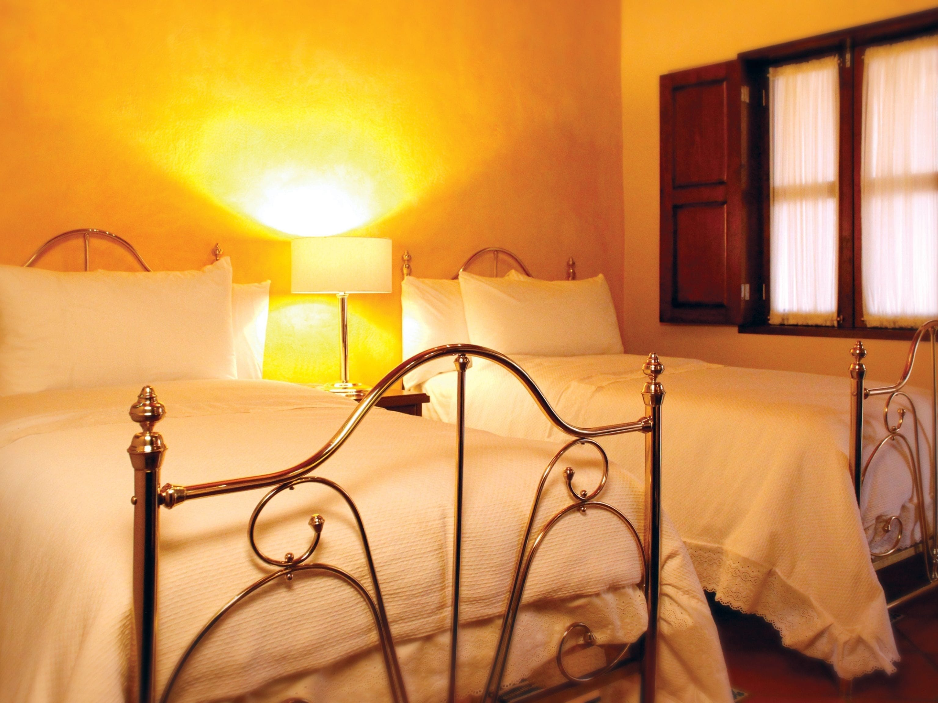 A hotel room with two beds, a nightstand with a lamp, and a window with curtains.