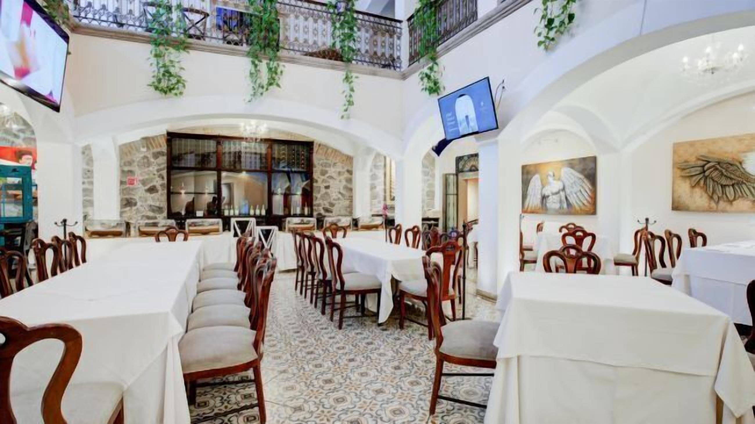 Restaurante com toalhas de mesa brancas, cadeiras de madeira e chão estampado.