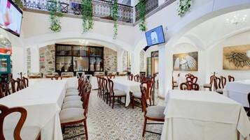 Restaurante com toalhas de mesa brancas, cadeiras de madeira e chão estampado.