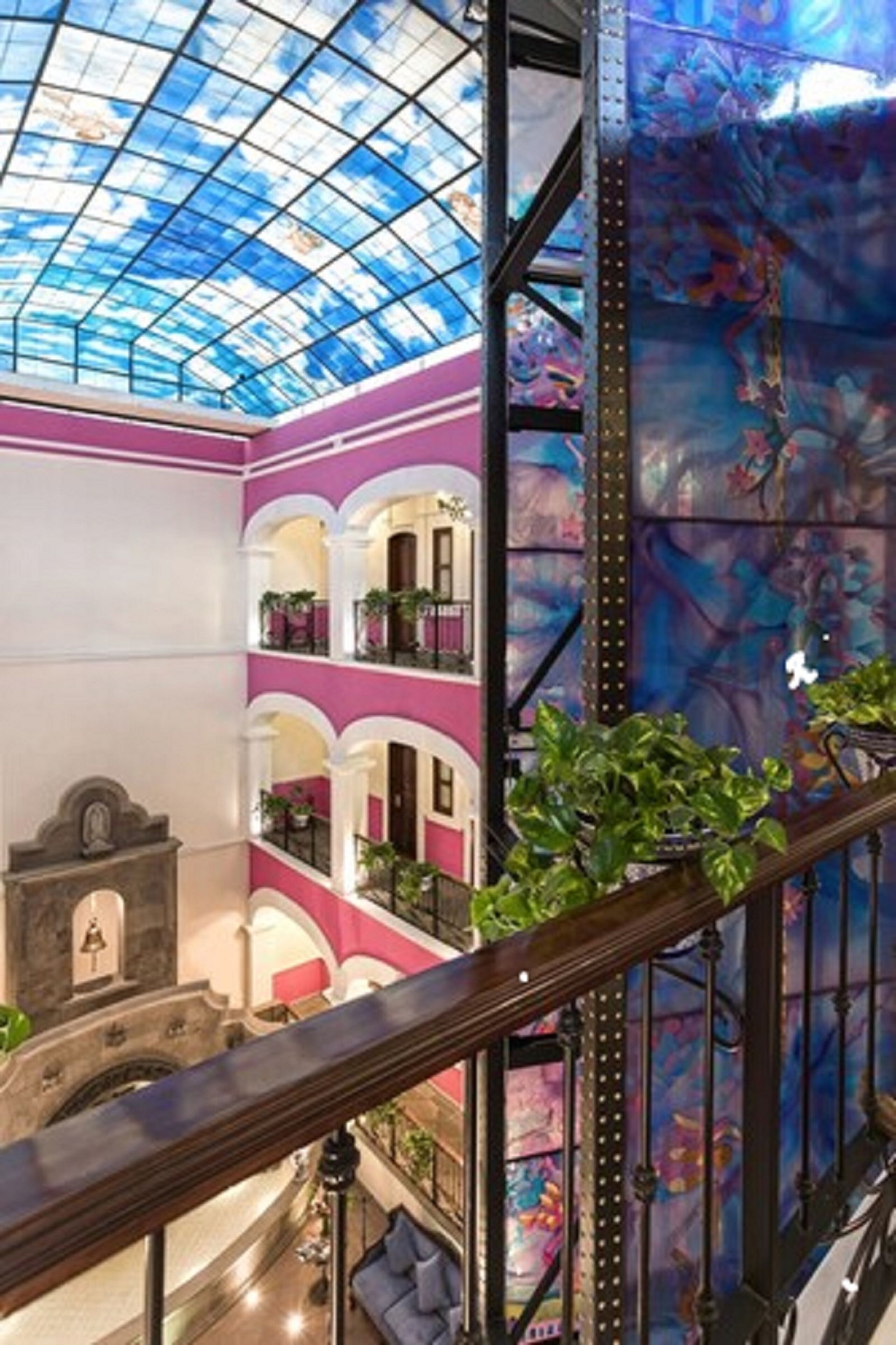 A multi-level atrium with a glass ceiling, pink and white walls, and balconies with plants.
