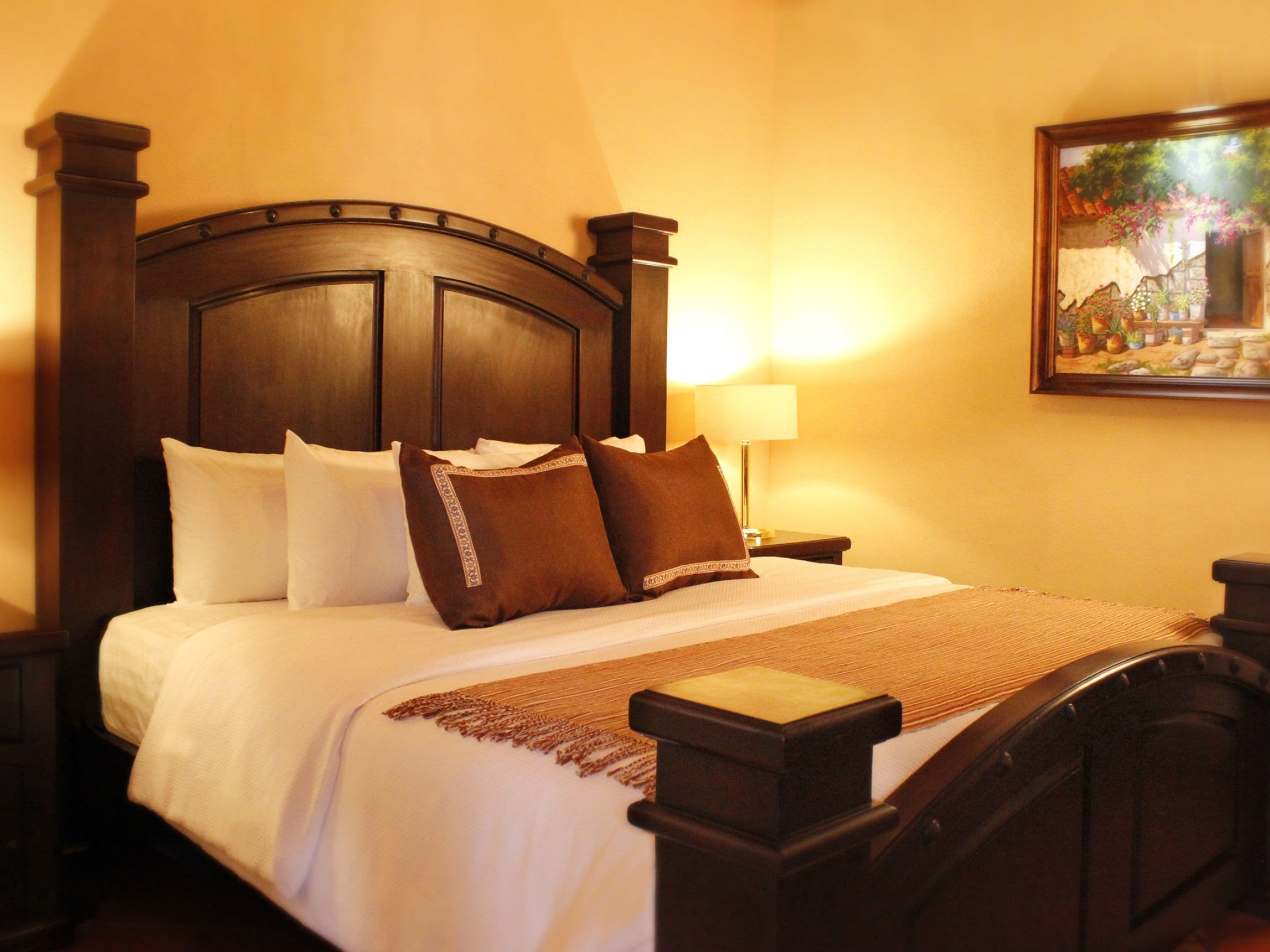 A neatly made bed with white and brown linens, a wooden headboard, and a bedside table with a lamp.