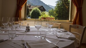 Une table à manger dressée, avec des verres à vin et des couverts, donnant sur un paysage montagneux.