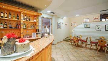 A restaurant with wooden shelves of bottles, a counter with cakes, and a dining area with chairs and tables.